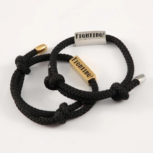 Detail von handgewebten schwarzen Seilarmbändern mit gravierten Metallwürfeln in Gold