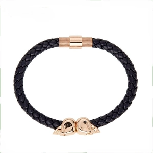 Detail of black braided leather bracelet featuring rose gold skull charms and magnetic clasp