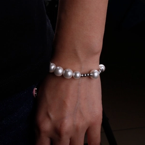 Close-up of minimalist pearl bracelet with silver metal beads worn on wrist with dark background