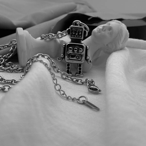 Detailed close-up of retro robot pendant on vintage steel chain over classical sculpture