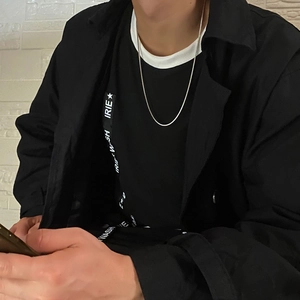 Close-up of a minimalist silver square snake chain necklace worn over a black t-shirt