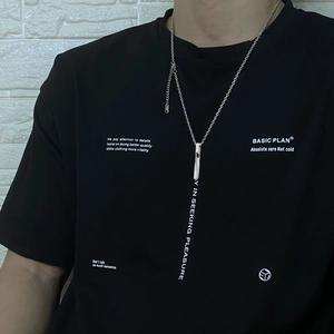 Collier avec pendentif cylindrique argenté porté sur un t-shirt noir pour un style moderne