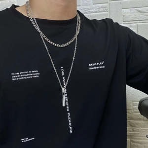 Détail de colliers superposés en acier titane avec pendentif cylindrique et chaîne gourmette