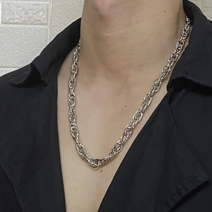 Detail view of a thick silver twisted chain necklace worn over a black shirt on a model