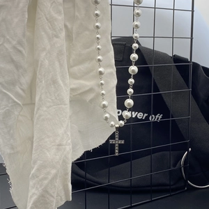 Detail of pearl necklace with sparkling rhinestone cross pendant on black wire mesh
