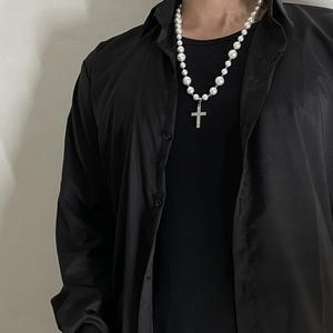 Detail of hip hop pearl necklace with a silver iced out cross pendant on black outfit