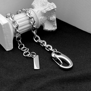 Polished silver cuban link bracelet with large carabiner clasp on white sculpture base