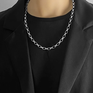 Nahaufnahme einer silbernen Unisex-Vierkantgliederkette über schwarzem T-Shirt und Blazer