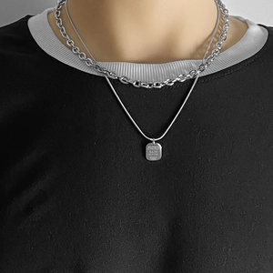 Détail de chaînes superposées en acier inoxydable avec pendentif carré sur un mannequin