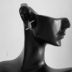 Punk style silver barbed wire stud earrings in stainless steel on a model