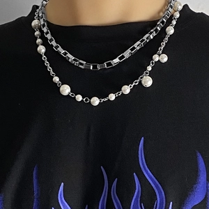 Detail of layered box chain and pearl necklace set on casual street style outfit