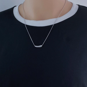 Close-up of minimalist silver titanium steel snake chain with curved cylinder pendant
