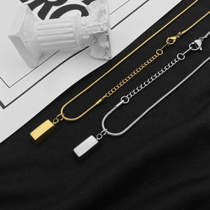 Dettaglio di pendenti rettangolari in oro e argento su sottili catene a maglia serpente