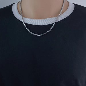 Detailed close-up of a silver geometric cube link chain necklace on a black shirt
