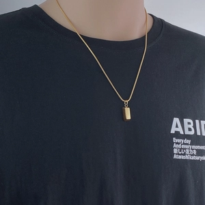 Dettaglio di un ciondolo rettangolare dorato minimalista su una collana a maglia snake