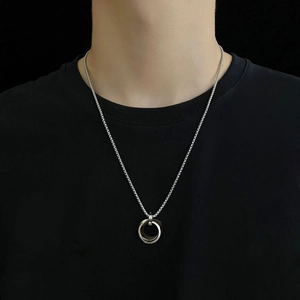 Détail du collier à pendentif triple anneau argenté sur fond de tissu noir pour homme