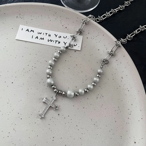 Détail du collier pendentif croix avec perles argentées et fausses perles sur assiette