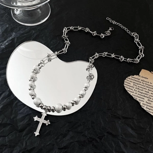 Détail du collier pendentif croix avec perles et chaîne argentée sur miroir en cœur