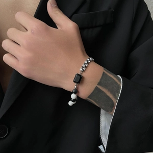 Close-up of black gemstone and zircon bracelet worn over a black suit sleeve