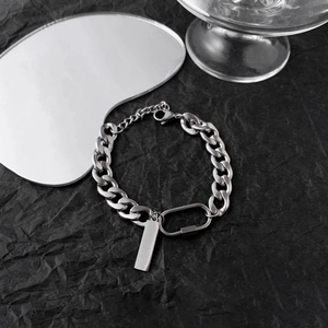 Macro detail of silver stainless steel Cuban chain bracelet with rectangular tag on black texture