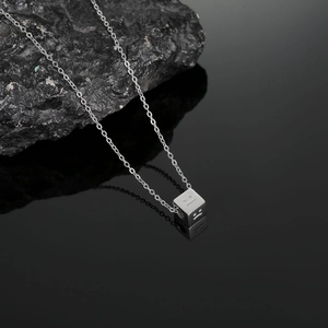 Detailed view of silver titanium steel emoji pendant on a sleek chain over dark rocks