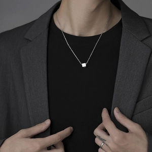 Detailed close-up of a square smiley pendant necklace on a silver chain worn by a male model