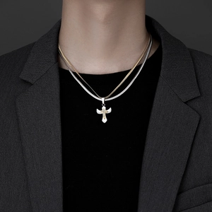 Detail of a double-layered necklace featuring a silver wing and golden cross pendant