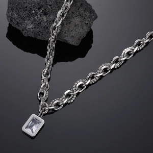 Detail of silver necklace with double chain and rectangular clear gemstone on dark stone