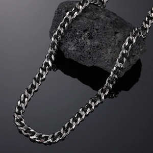 Macro shot of men's silver stainless steel Cuban link chain on a textured black rock