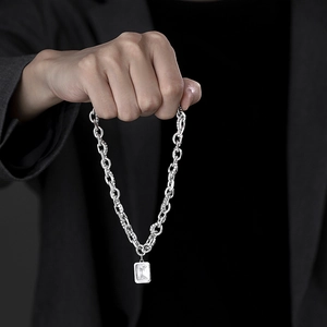 Detailed close-up of emerald-cut clear stone pendant on thick silver chain necklace