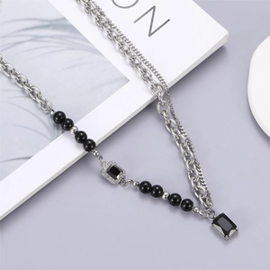 Double-layered titanium steel necklace with black gemstones and pearls on a magazine