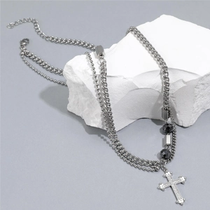 Detailed close-up of double-layer titanium necklace with rhinestone cross on white rock