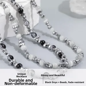 Detail of beaded necklace with grey hematite and white cat eye stones on a rock