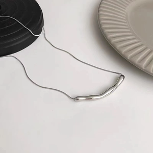 Detailed view of irregular silver pendant with snake chain on a minimalist display