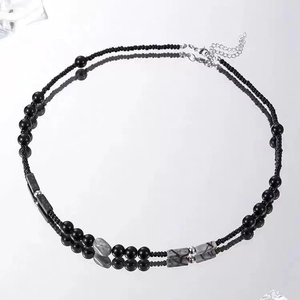 Minimalist beaded necklace with black beads and marble accents on a mirror surface