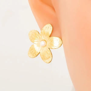 Gold floral stud earring with textured metal petals and central pearl on model