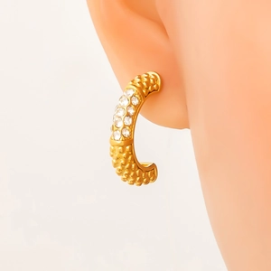 Macro view of gold C-shaped earring with sparkling zircons and textured metal finish