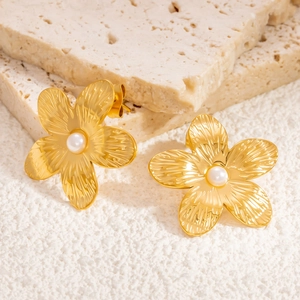Macro detail of gold flower earrings with ribbed petals and center pearl on stone