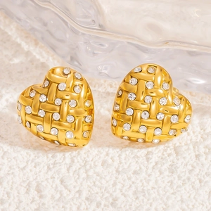 Detailed macro view of heart-shaped gold earrings with braided texture and zircon inlay