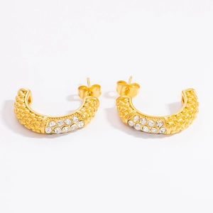 Macro detail of gold C-shaped hoop earrings with textured finish and sparkling rhinestones