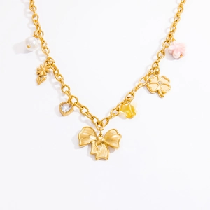 Détail du collier plaqué or 18k avec perles, nœud et breloques florales sur fond blanc