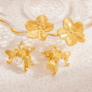 Gros plan de boucles d'oreilles fleur et abeille dorées avec perle blanche et métal brossé