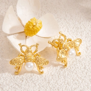 Gros plan détaillé de boucles d'oreilles abeille en or 18K avec perles sur tissu