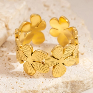 Macro shot of gold floral open ring with textured petals on a beige stone surface