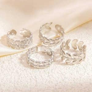 Set of four silver stainless steel leaf pattern open rings on a silk fabric background