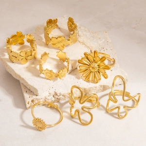 Golden stainless steel ring set featuring daisy and butterfly motifs on stone surface