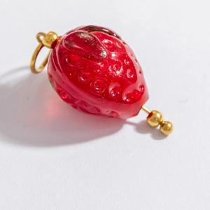 Vue détaillée d'un pendentif fraise en verre rouge avec apprêts dorés pour bijoux DIY