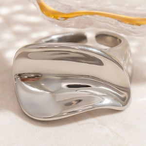 Macro detail of irregular wave-shaped liquid metal silver ring on a decorative background