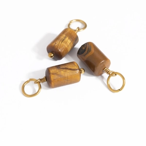 Detailed macro view of natural tiger eye cylindrical stone pendants with gold metal rings