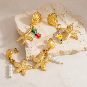 Boucles d'oreilles étoile de mer et coquillage dorées avec perles sur plateau pierre